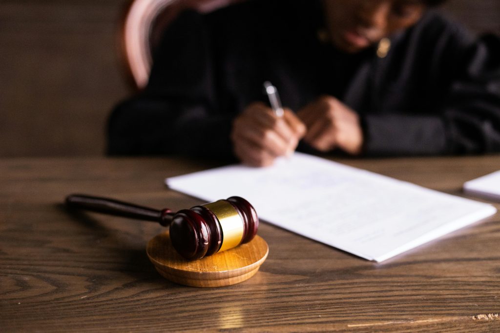 pexels-photo-6077447-6077447 Judge signing documents at desk with focus on gavel, representing law and justice.